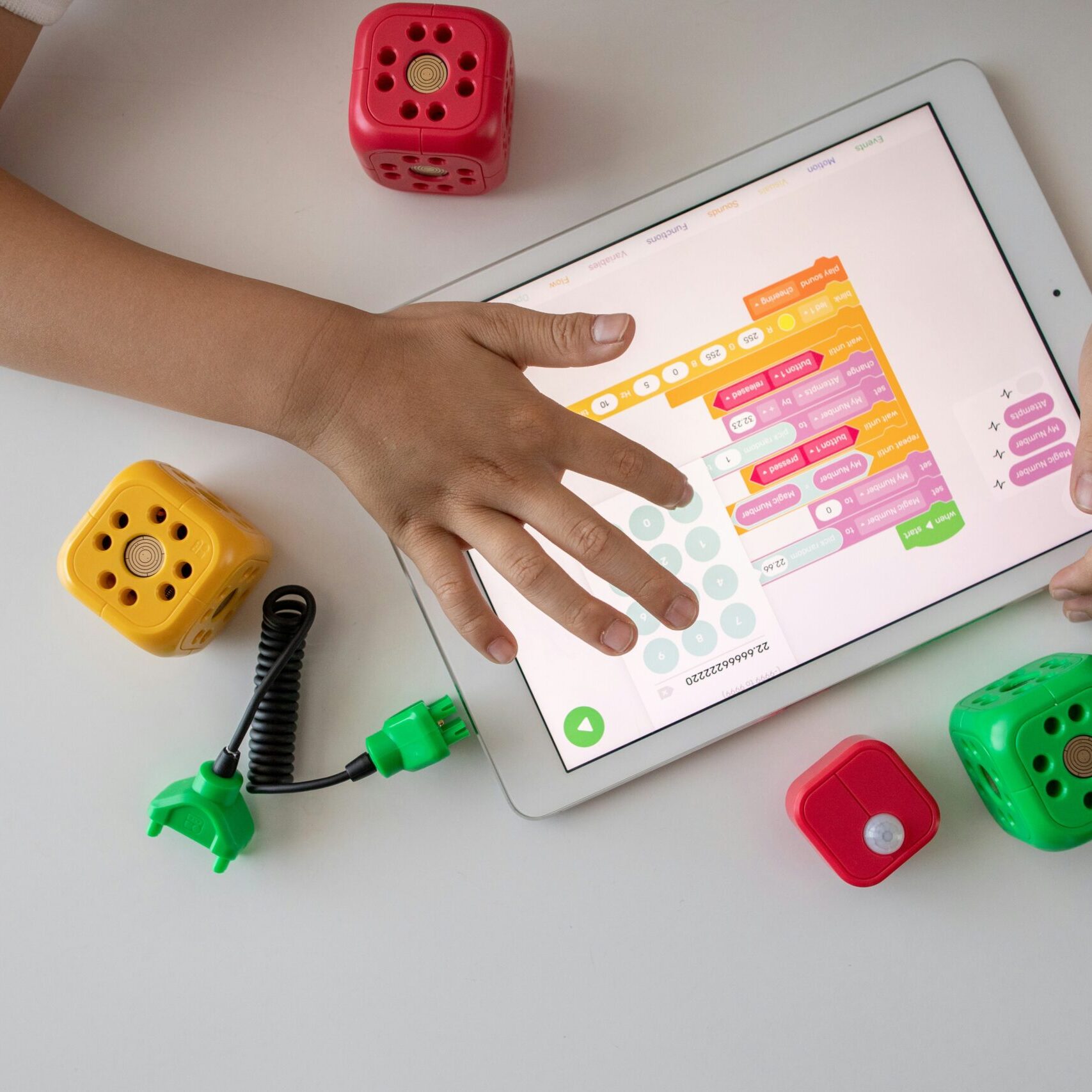 Top-view image of a child playing an educational game on a tablet, with block toys scattered around